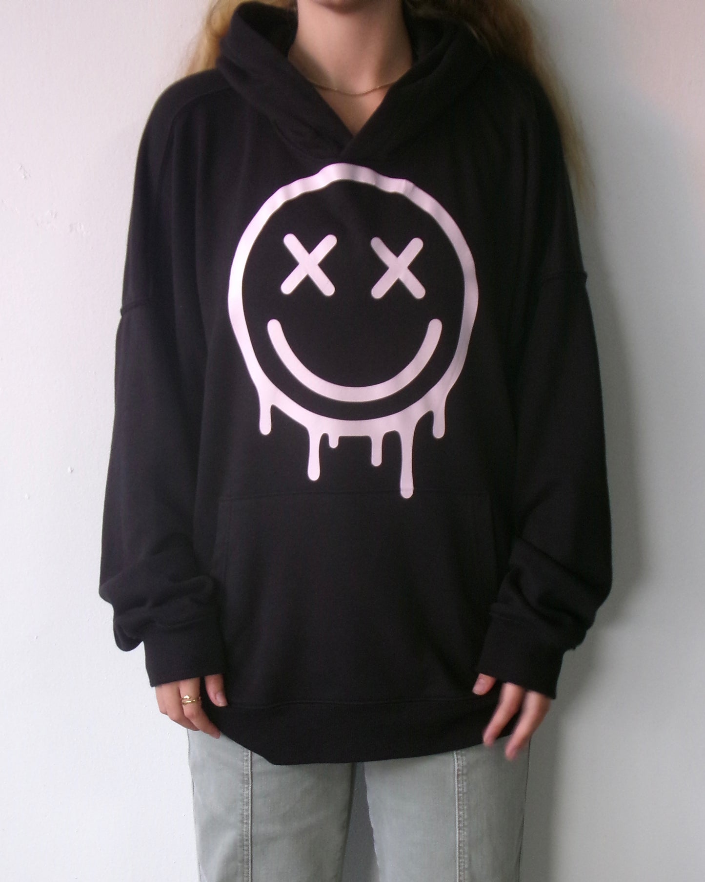 Front of the OUTSPOKEN Signature Hoodie in black with pink dripping smiley graphic